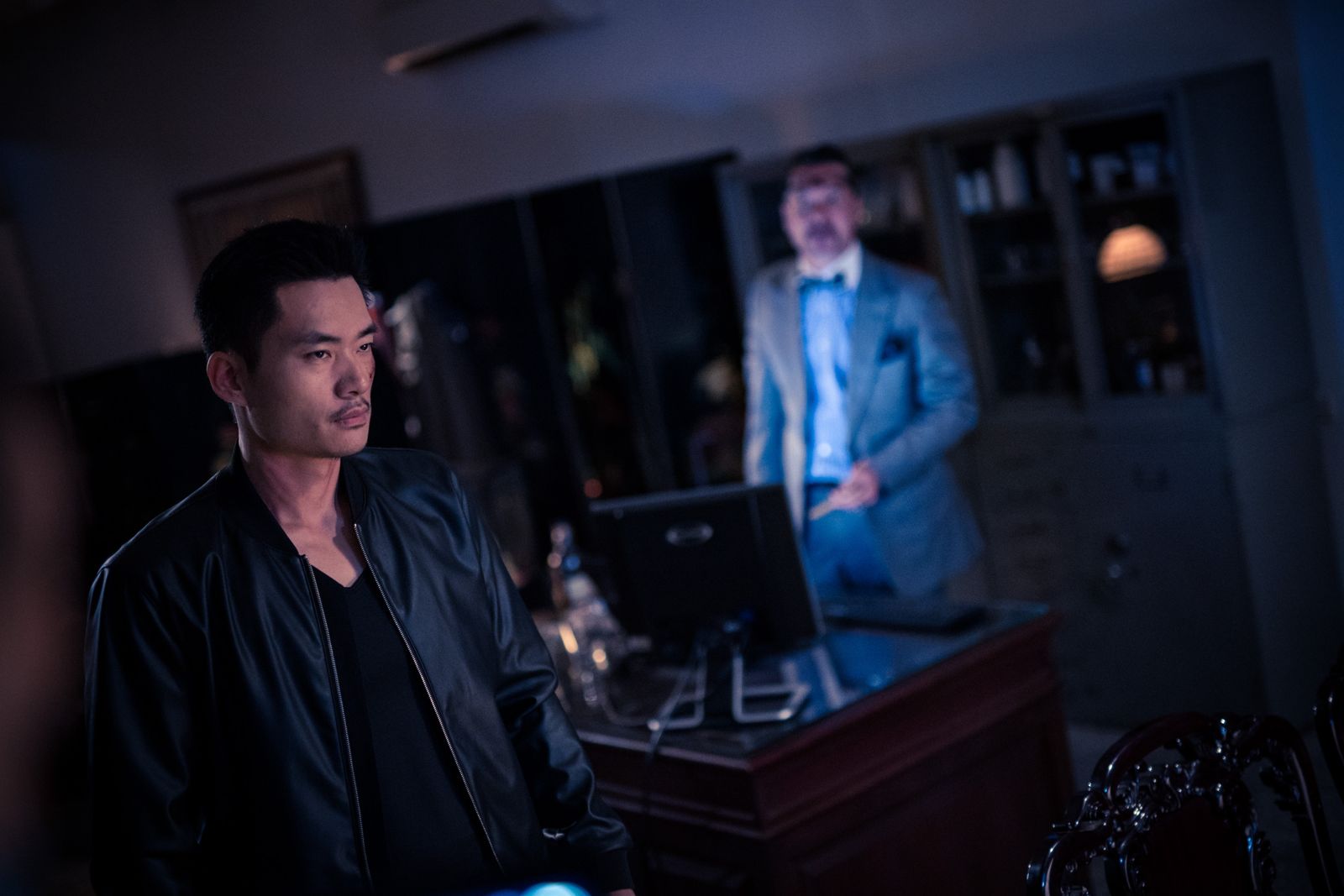 Kuang Feng in a dim office with a man behind a desk
