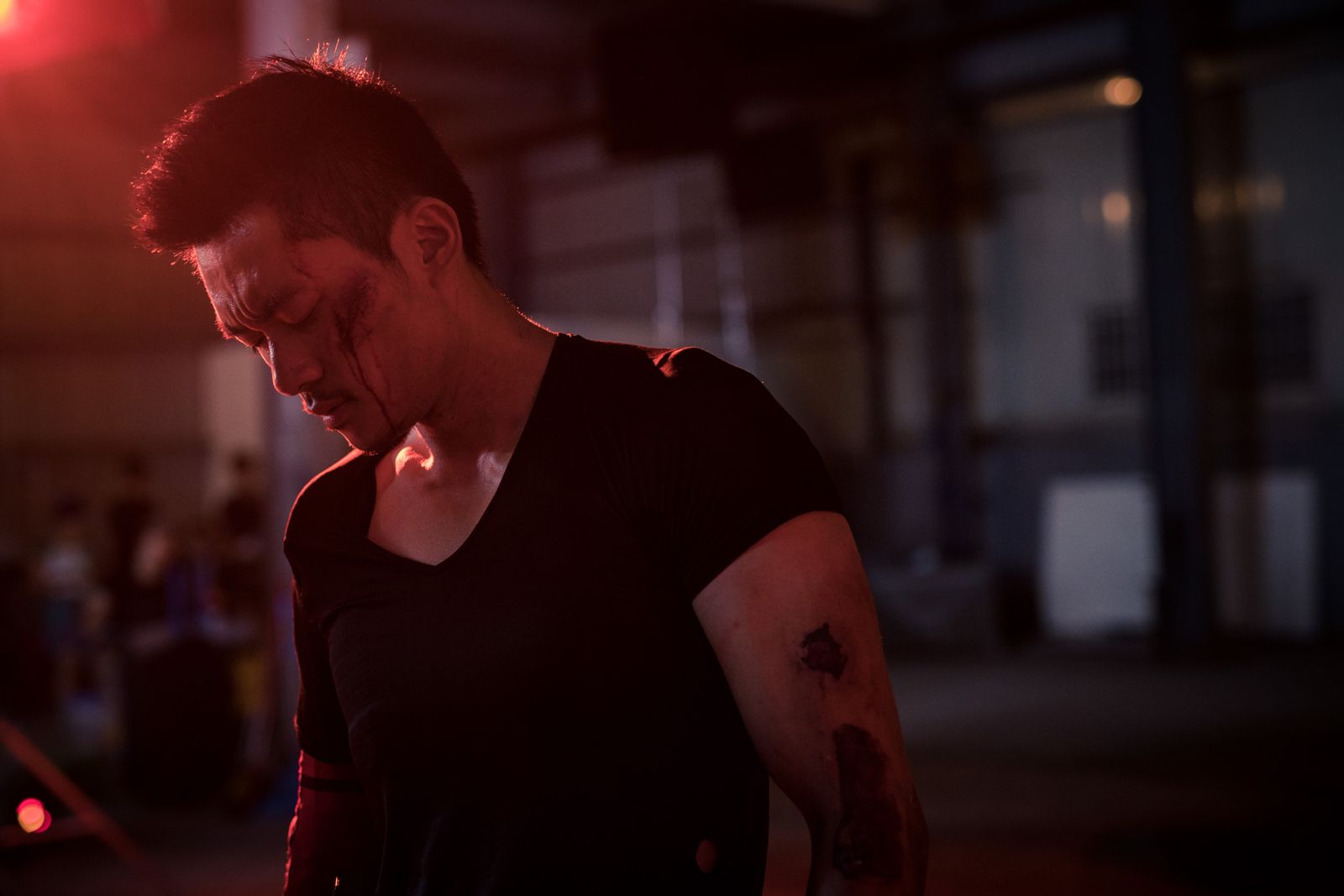 Kuang Feng with his head down, backlit in red