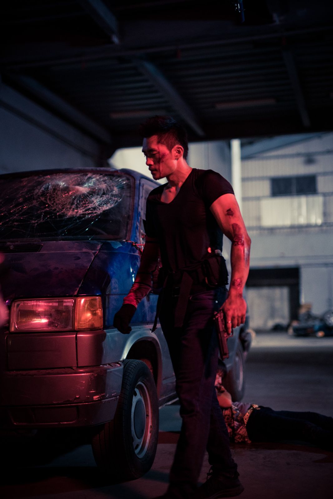 Kuang Feng walking past a wrecked van with a pistol